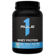 Black protein powder jar with a blue RULE 1 WHEY PROTEIN label and light blue Birthday Cake flavor icon