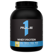 Large black protein powder jar with a blue RULE 1 WHEY PROTEIN label and yellow Banana Creme flavor icon